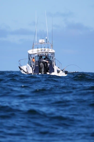 Fishing boat with two anglers engaged in fishing on the ocean, surrounded by water and clear skies.