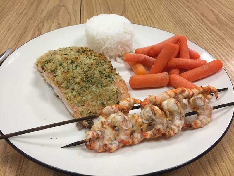 Plate with baked salmon fillet, white rice, steamed carrots, and shrimp skewers arranged on a round dish.