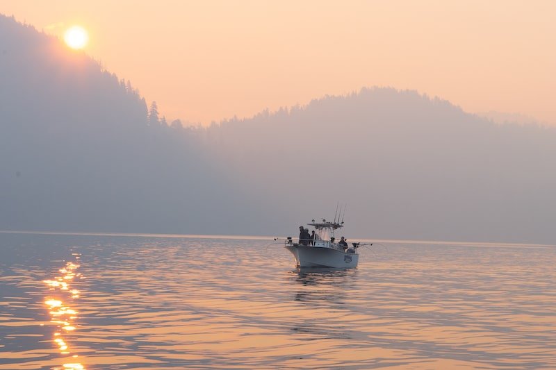 Fishing boat on calm water during sunset with hazy mountains in the background.