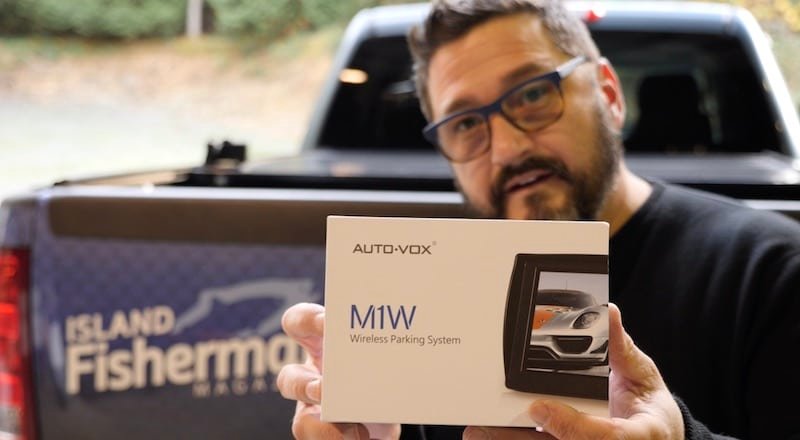 A person holding a box labeled 'AUTO-VOX M1W Wireless Parking System' with an image of a car on the packaging.