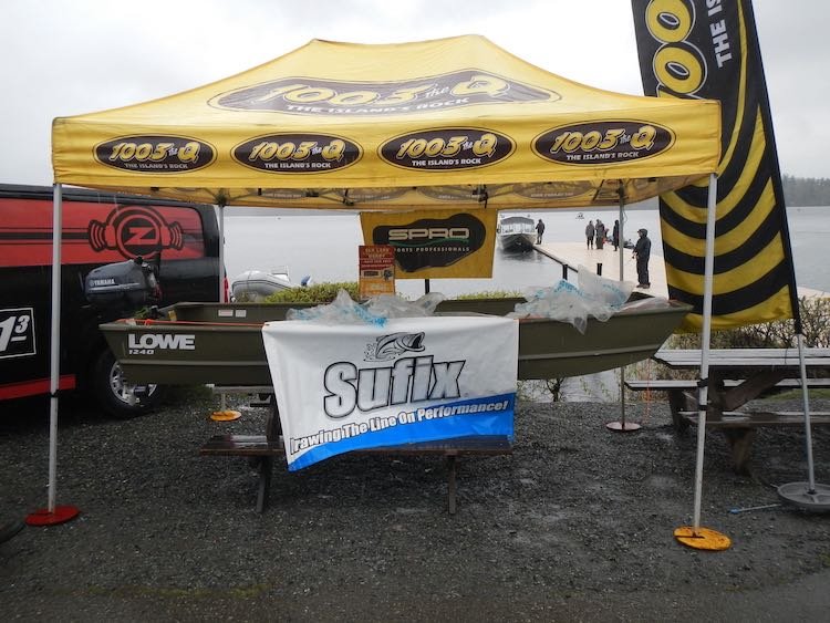 Lowe boat displayed under a promotional tent with branding for 100.3 The Q and Sufix, set at a waterfront location.