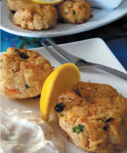 Two crab cakes garnished with lemon wedges and served with a side of tartar sauce on a white plate.