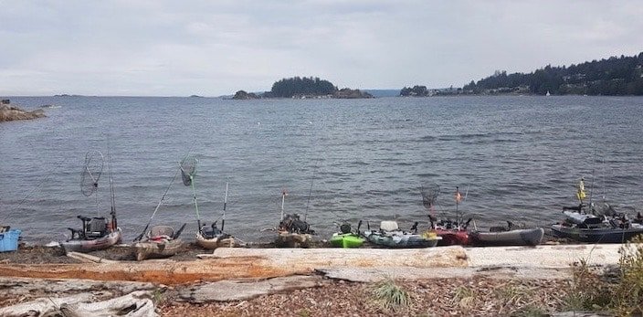 Several fishing kayaks lined up along the shoreline with a calm water backdrop and distant islands visible.