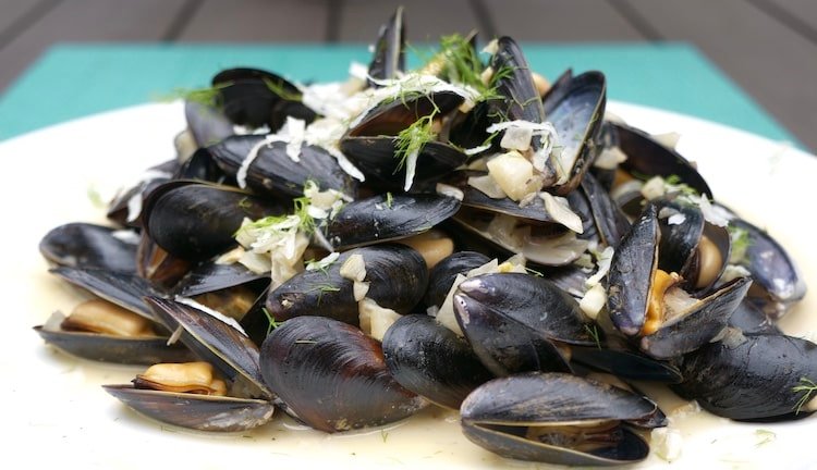 Plate of cooked mussels garnished with herbs and garlic, presented in a neat arrangement.