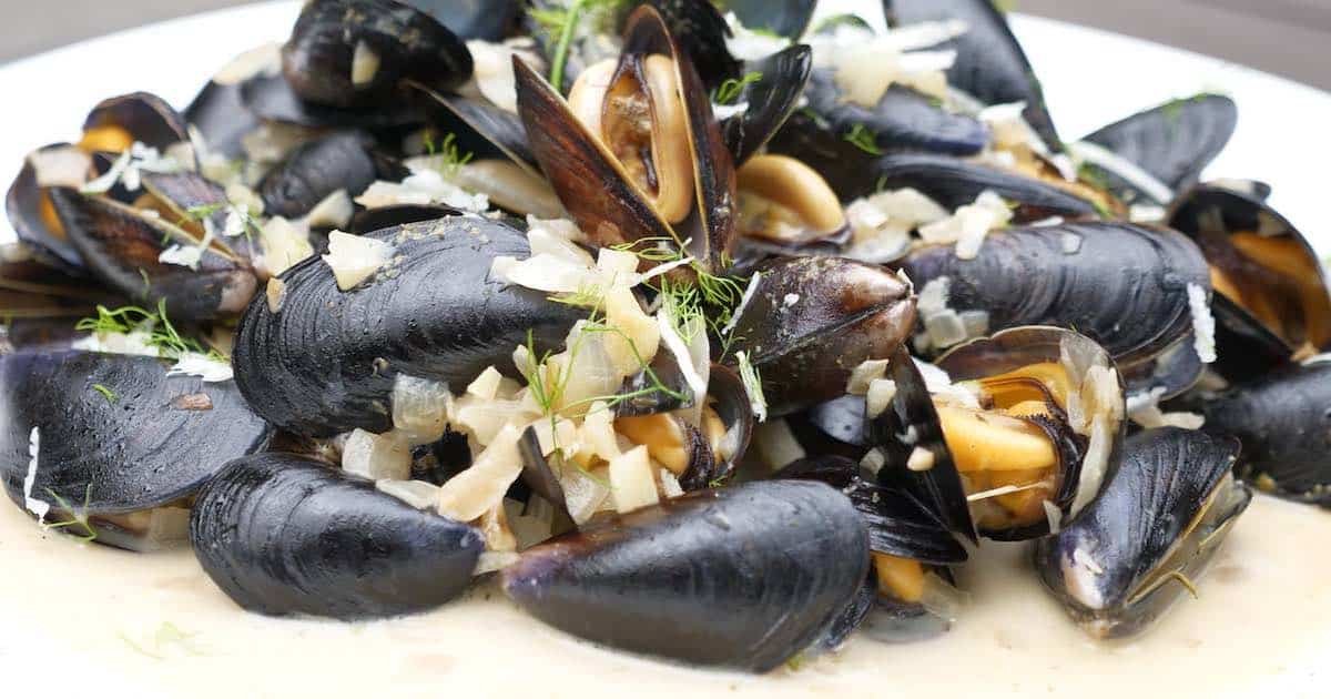 A plate of mussels cooked with herbs and garnished with chopped onions and spices, presented in a creamy sauce.