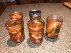 Five glass jars filled with pickled salmon, featuring layers of fish, spices, and herbs in a reddish liquid.