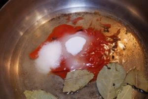 Ingredients for pickled salmon including red sauce, salt, and bay leaves in a metal pan.