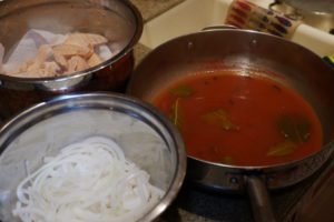 Preparation ingredients for pickled salmon, including salmon pieces, a pot with tomato sauce and bay leaves, and sliced onions in a bowl.
