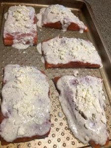 Five pieces of salmon fillets topped with a creamy feta cheese sauce on a baking tray.