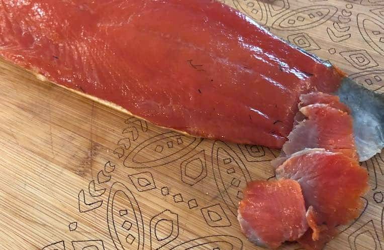 Sliced lox on a wooden cutting board, with a portion cut away from the main piece, showcasing its smooth texture and rich color.