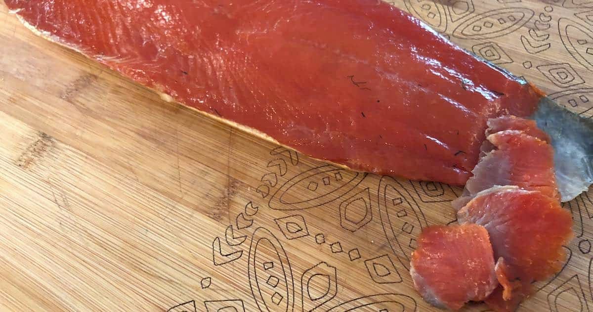 Sliced smoked salmon on a wooden cutting board, with a portion of the fish cut into smaller pieces.