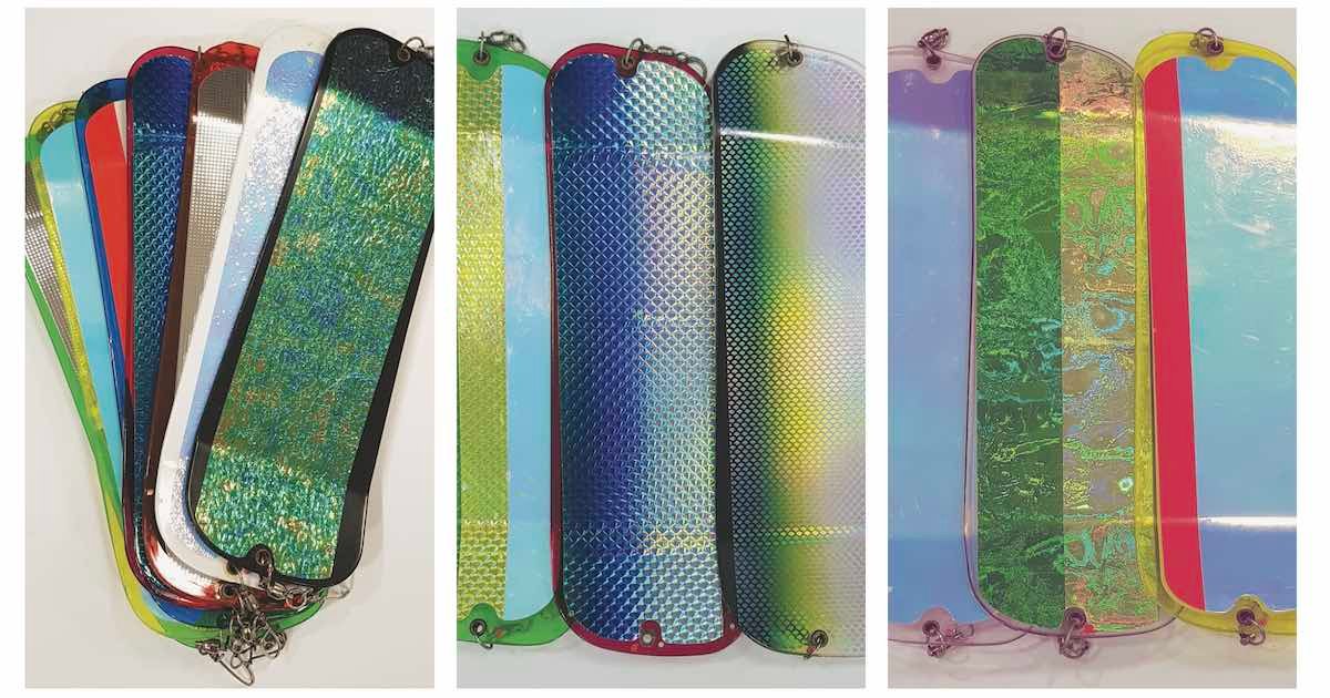Collection of fishing flashers in various colors and patterns, including reflective and holographic surfaces, arranged in a fan shape.