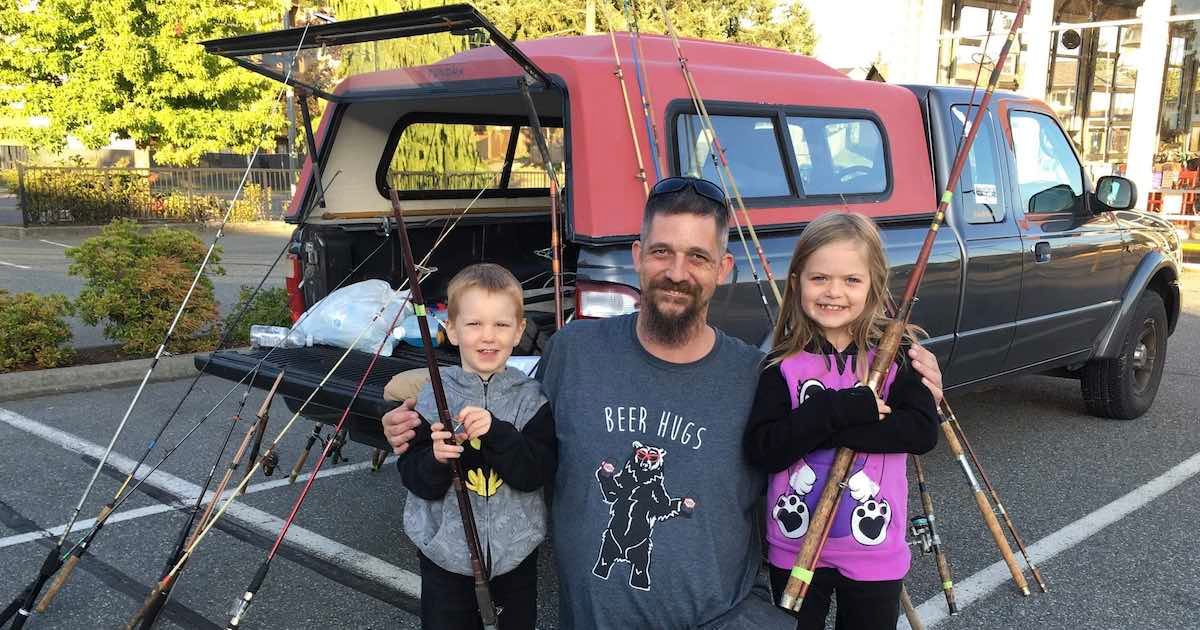 Two children and an adult holding fishing rods in front of a pickup truck with a camper shell.