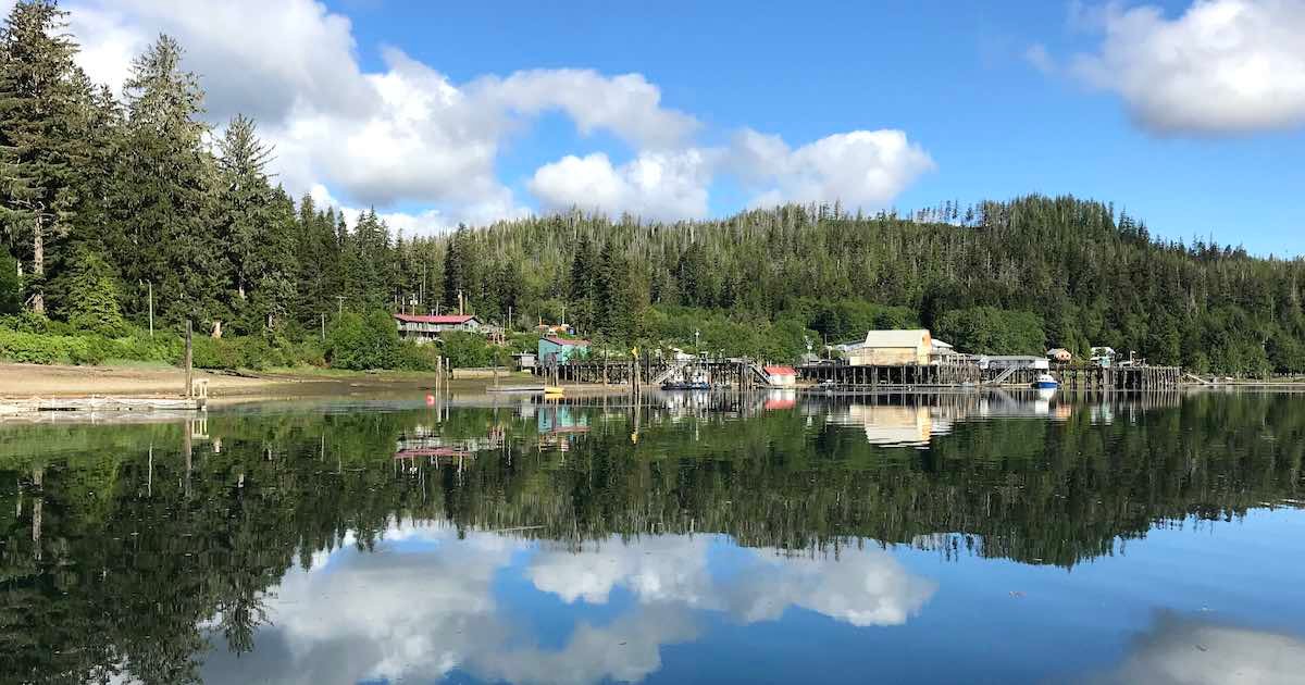 Calm water reflecting a dock and buildings surrounded by trees in Winter Harbour, British Columbia.