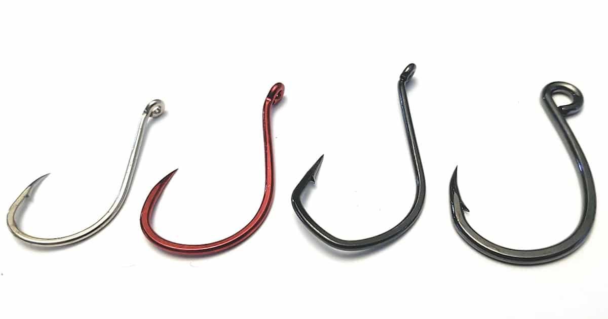 Four fishing hooks in varying colors: silver, red, and two black hooks, each with distinct shapes and sizes.