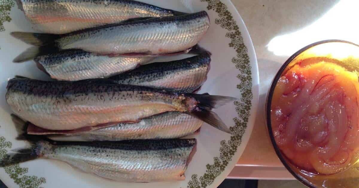 Five herring fish arranged on a plate next to a bowl of orange fish roe.