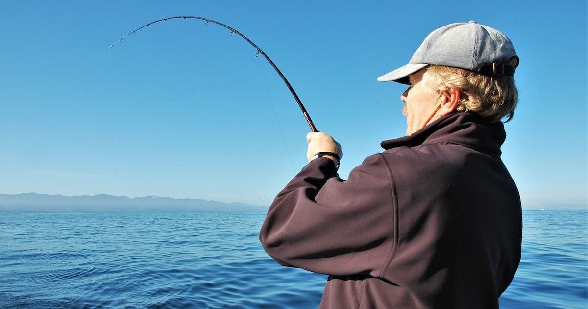 Person holding a fishing rod with a bent line, indicating a catch, against a calm ocean backdrop.