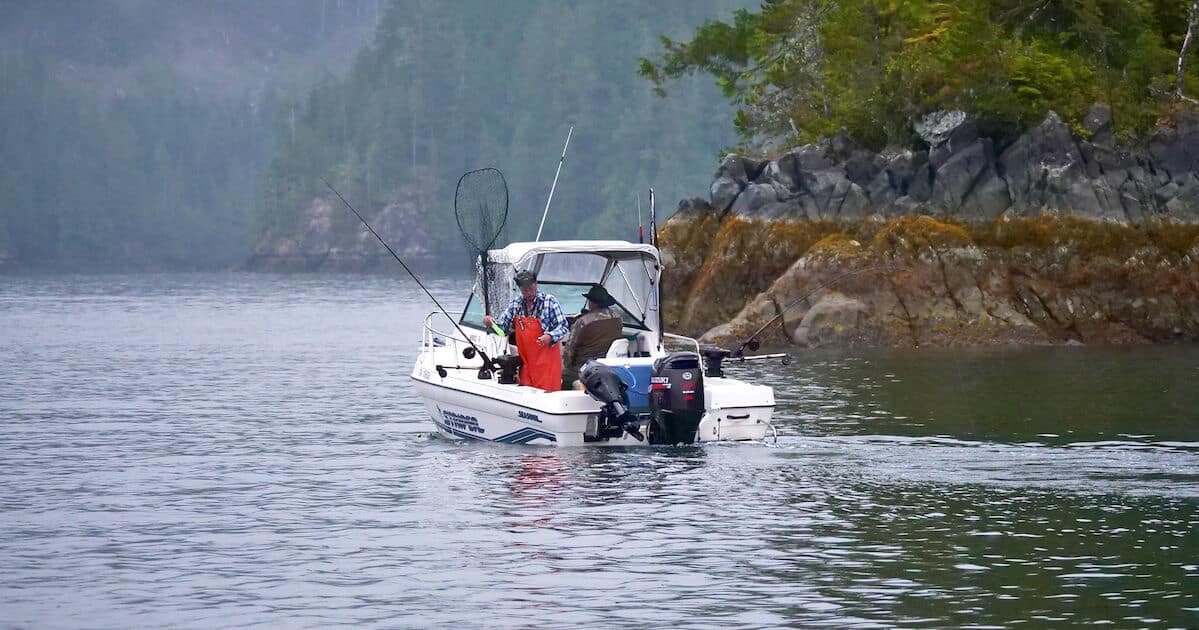 Fishing boat with anglers preparing to fish in calm waters surrounded by rocky terrain and trees.