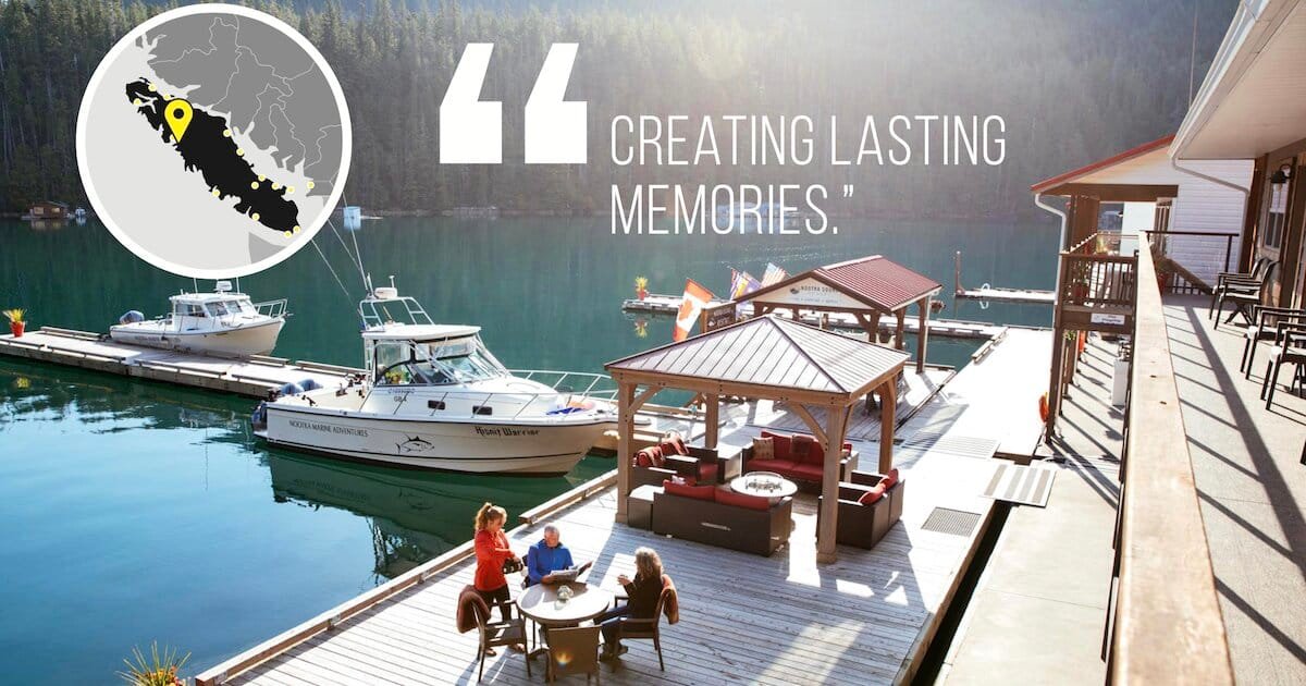 Boats docked at a marina with people gathered around a seating area on a wooden deck overlooking calm waters.