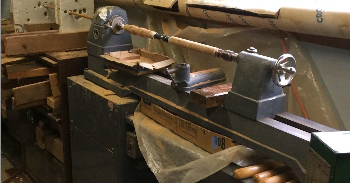 Woodworking lathe with a wooden rod positioned for shaping in a workshop setting.