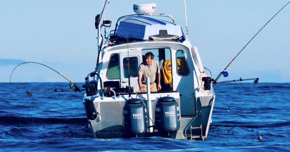 Fishing boat with two outboard motors and a person sitting on the deck, engaged in fishing activities on the water.