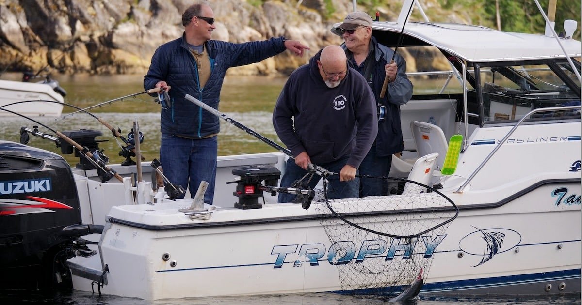 Three men on a fishing boat named 'Trophy' preparing to catch fish with nets and fishing rods in a coastal setting.