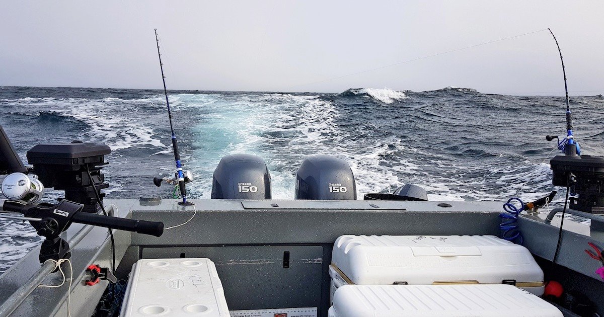 Two outboard motors on a fishing boat with fishing rods positioned on the sides, navigating through choppy ocean waters.