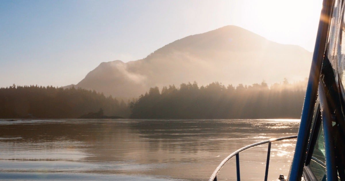 View of a mountainous landscape with soft sunlight reflecting on calm water, captured from a boat's perspective.