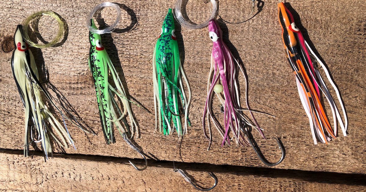 Five colorful salmon lures with various designs, including green, purple, and orange, displayed on a wooden surface.