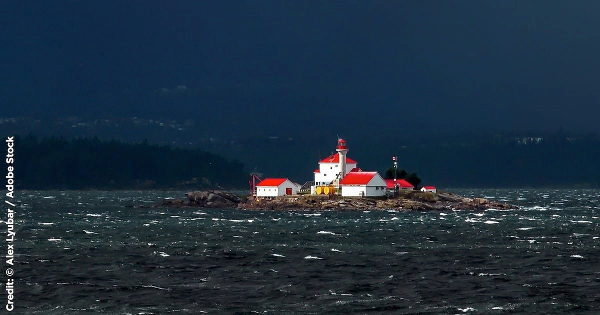 Lighthouse on a rocky island with a red roof, surrounded by turbulent waters under a dark sky.