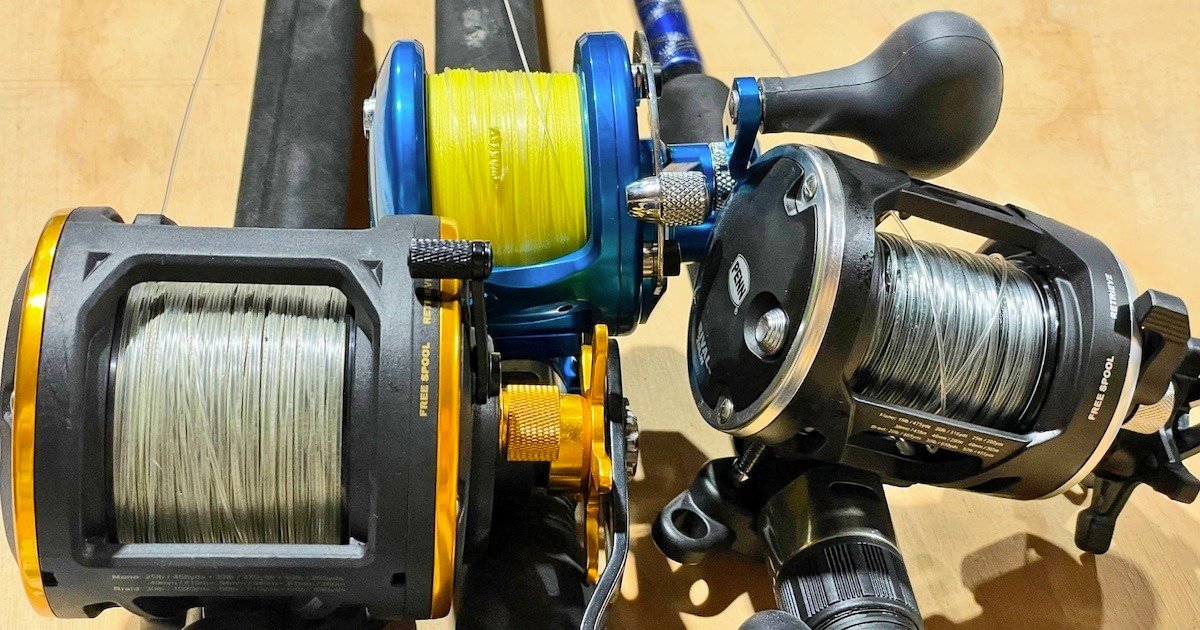Three fishing reels with different line types: one with yellow line, one with silver line, and one with black detailing, arranged on a flat surface.