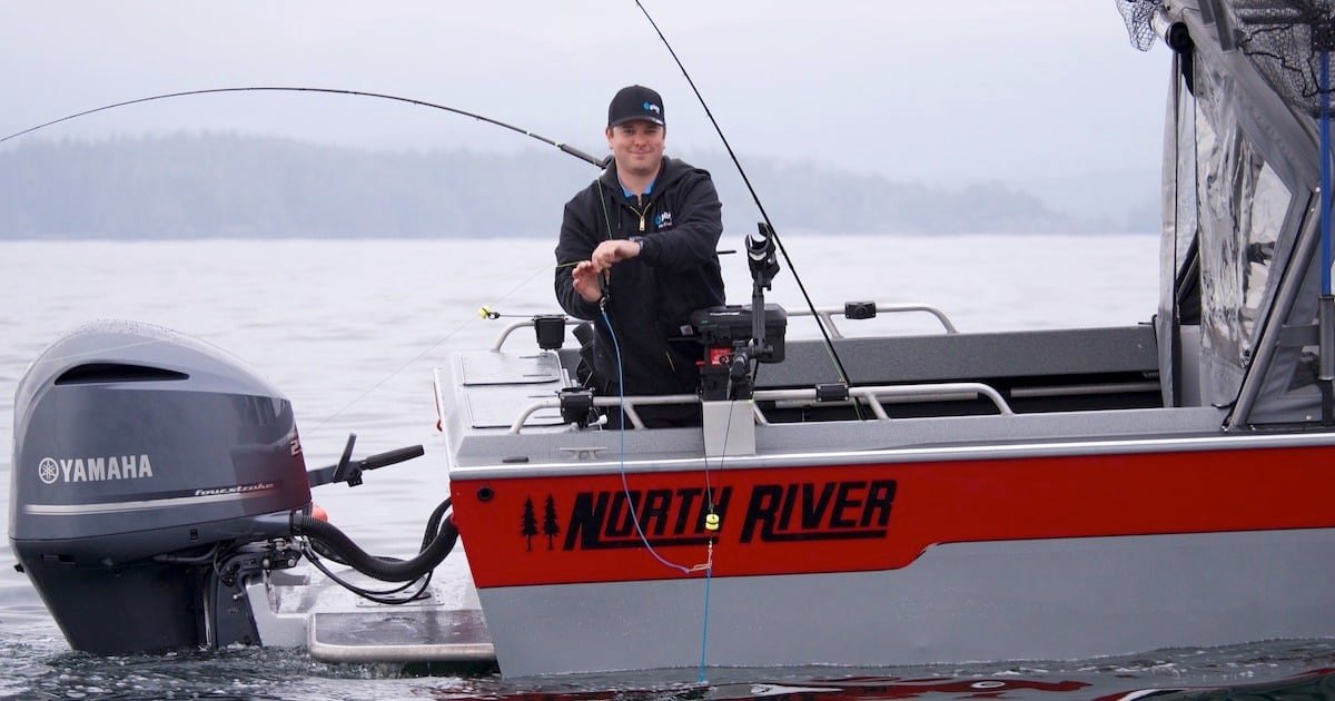 Man holding a fishing rod on a North River boat with a Yamaha motor in a calm water setting.