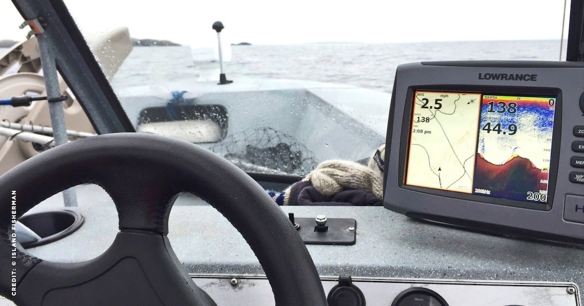 Fish finder display showing depth and water temperature on a boat's dashboard with steering wheel in view.