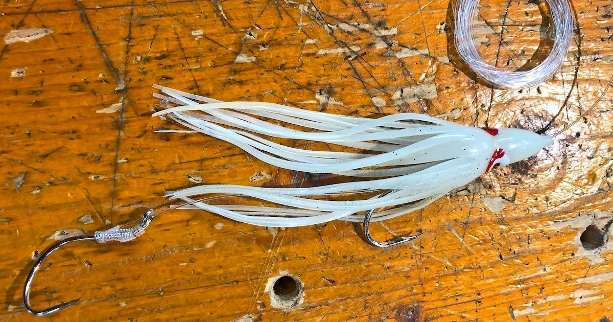 White fishing lure with tentacle-like strands attached to a metal hook on a wooden surface.
