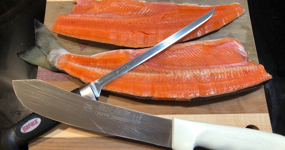 Two fillets of salmon on a wooden cutting board with a filleting knife and a boning knife placed on top.