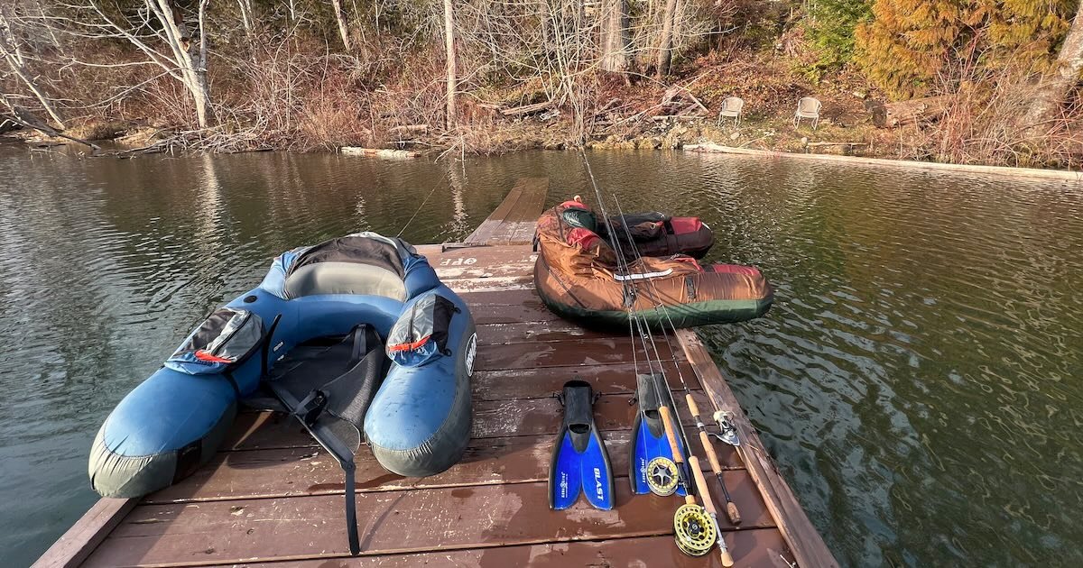 Two float tubes and fishing gear placed on a wooden dock by the water, with fishing rods and fins arranged beside them.