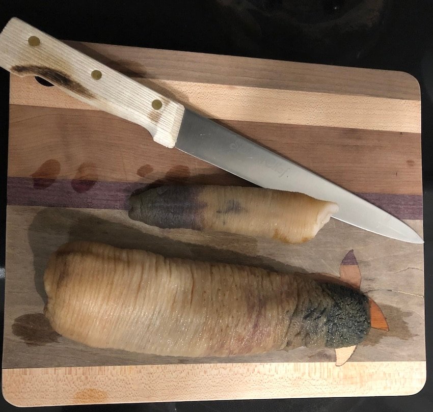Two fish fillets on a wooden cutting board with a knife placed beside them.