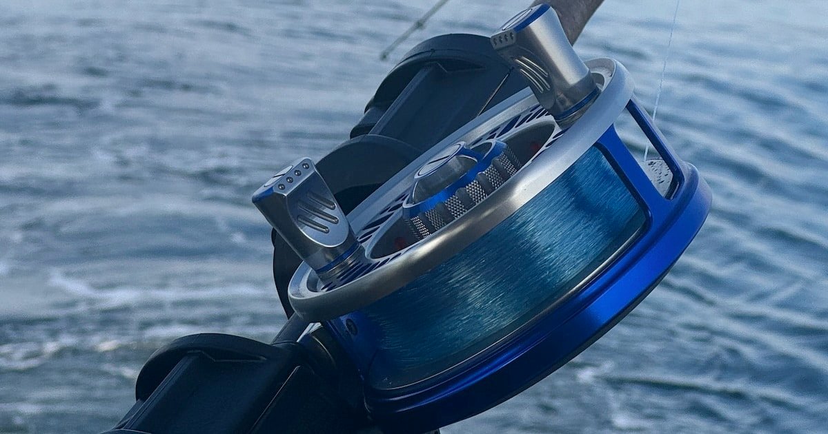 Close-up of a blue fishing reel mounted on a fishing rod, with a spool of line visible against a blurred water background.