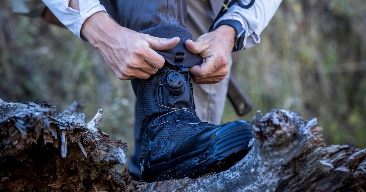 Person fastening the Boa lacing system on a black fishing boot while standing on a log.