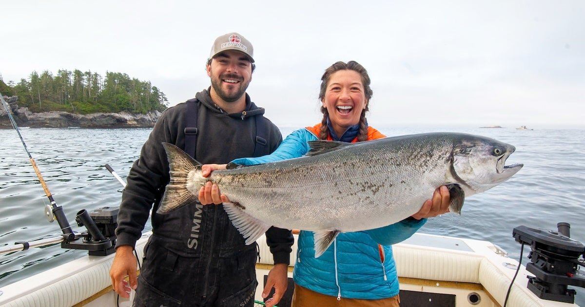 Two individuals holding a large Chinook salmon while on a boat in a marine environment.