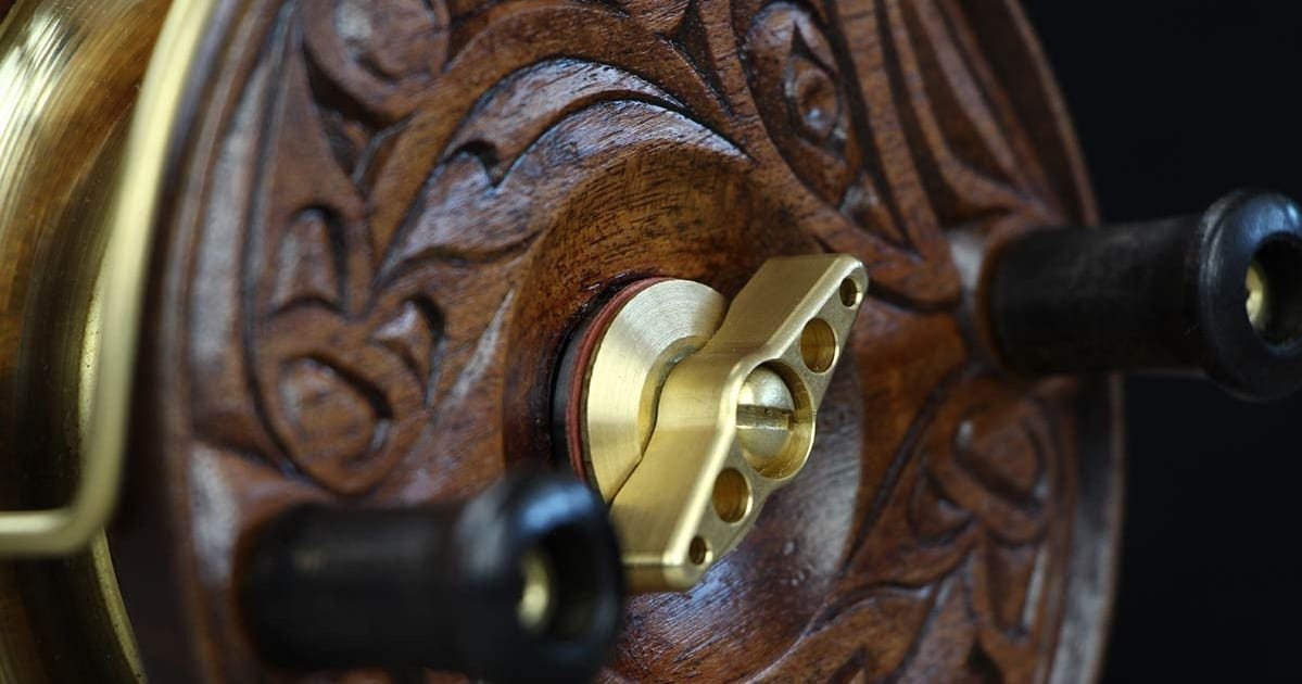 Close-up of a wooden fishing reel with intricate carvings and a brass handle, highlighting detailed craftsmanship.