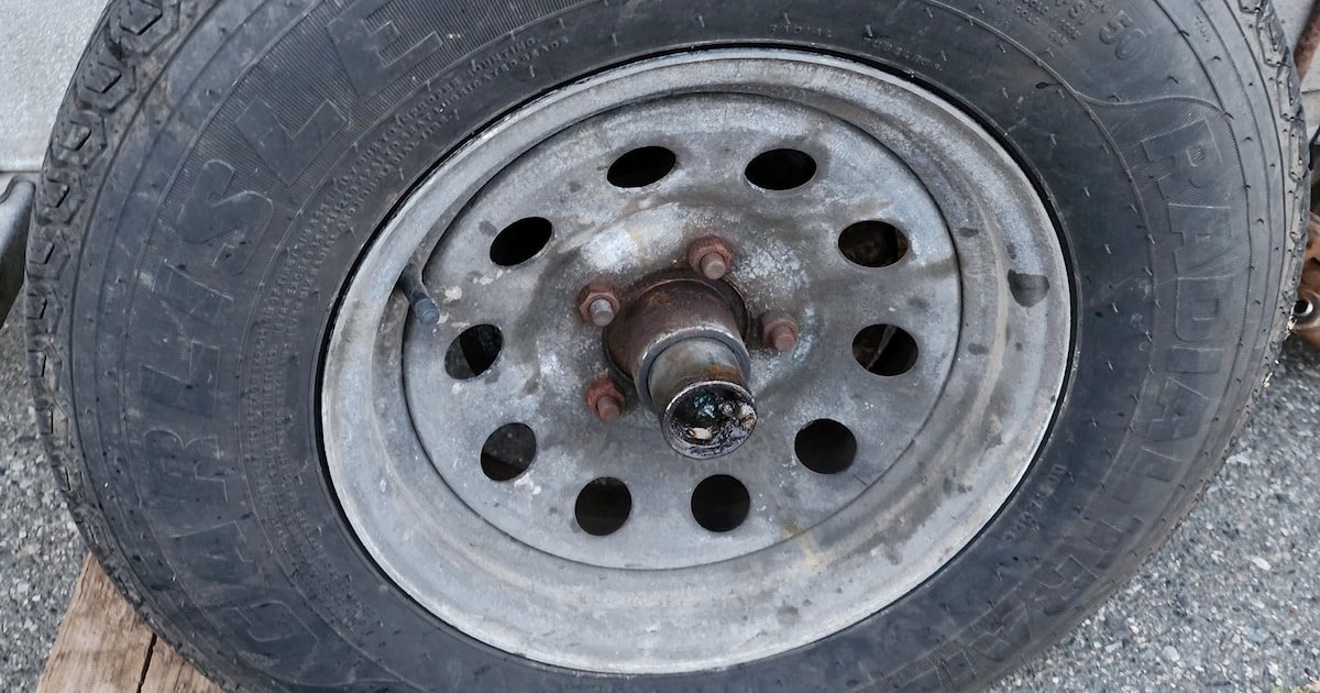 Close-up of a trailer wheel with a metal rim and tire, showing visible wear and rust on the hub and bolts.