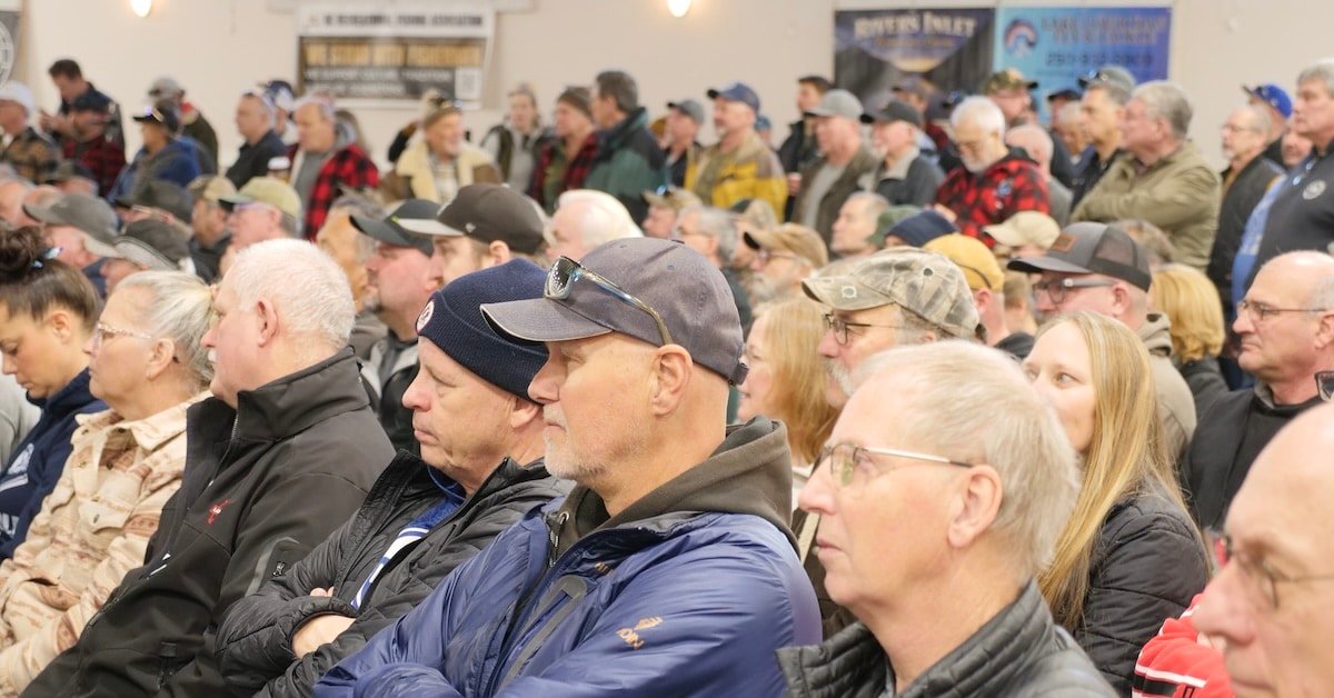 DFO Salmon Allocation Policy Crowd of people attending a town hall meeting, with individuals seated and focused on the speaker in a large indoor space.
