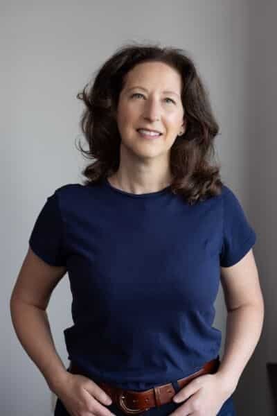 Alt Text: Tamara KronisA professional portrait of Tamara Kronis, the Member of Parliament for Nanaimo—Ladysmith. She is a woman with shoulder-length, wavy brown hair, looking directly at the camera with a slight smile. She is wearing a simple, short-sleeved navy blue t-shirt and a dark-colored pair of pants held by a brown leather belt. The photo has a soft, neutral-colored background.